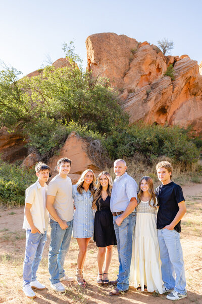 Blended family with older kids pose for a smiling portrait in front of Utah's beautiful red rocks.