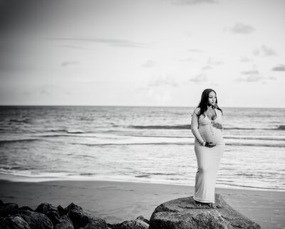Capture the beauty of motherhood with this image of a Black pregnant woman in a fitted white maxi dress from Naked Wardrobe, standing gracefully on Folly Beach. A perfect blend of elegance and serenity.