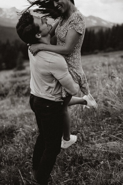 Groom lifts fiancée in a breezy mountain field during an adventurous Breckenridge engagement session.