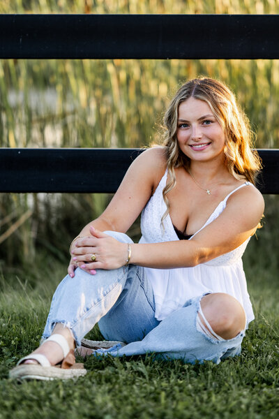 Senior girl poses against a fence in soft golden hour light during her senior portrait session