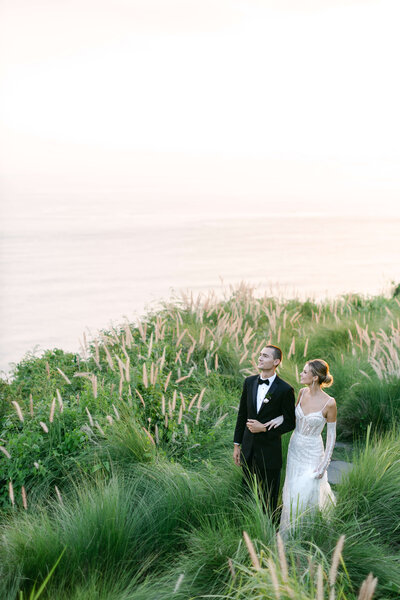 A bride and groom stare off cliffs overlooking the indian ocean.