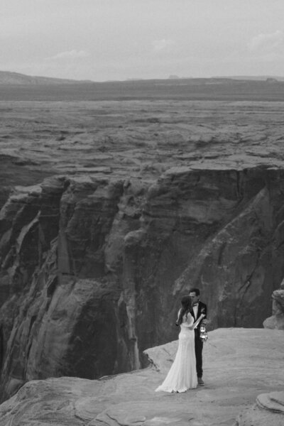 Elopement bij horseshoe bend in Arizona, USA. Het bruidspaar houdt lampjes vast en geeft elkaar een kus. Deze foto is in zwart wit en vastgelegd door Sharon Kastelijns Photography.