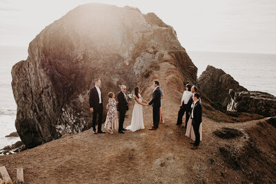 a bride stroking a groom's face while standing on a cliff side