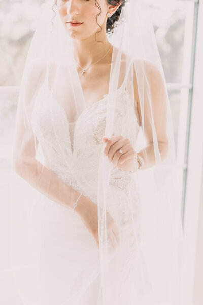 bride in white dress holding veil in hand