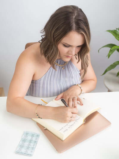 woman sitting at a white desk writing in journal