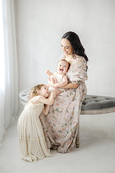 Adorable 6-month milestone portrait of baby boy, mother and big sister in Tampa studio with soft natural lighting and neutral backdrop