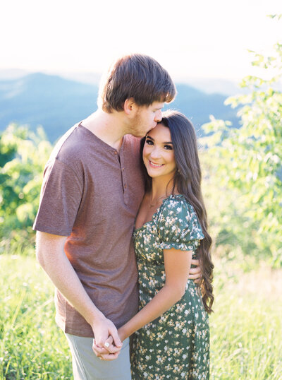 Fiance kissing the forehead of his future wife in a field