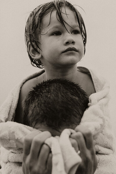 Sunshine Coast photographer capturing a black-and-white storytelling portrait of a young boy wrapped in a towel on his father's shoulders