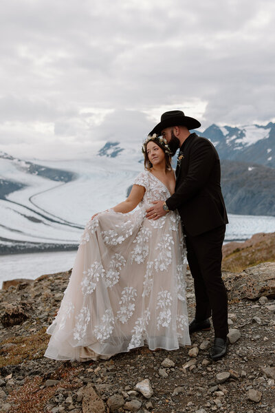 Elopement couple embraces with bride fanning dress on glacier.

