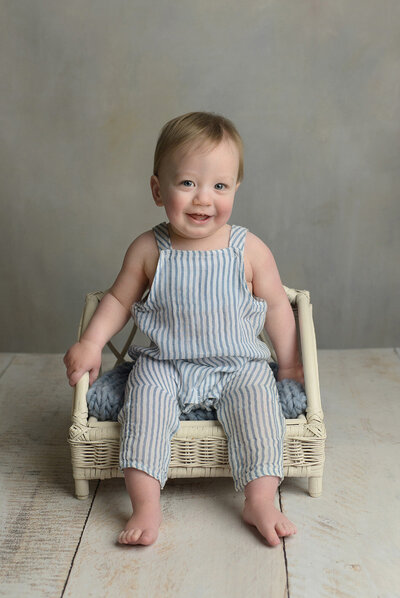 smiling one year old boy sitting on a white bench