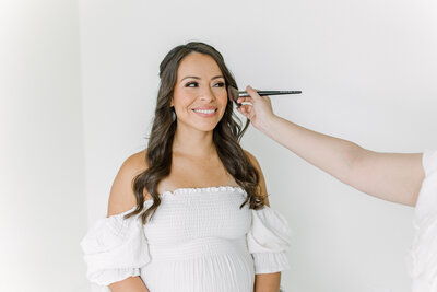 Maternity Photographer, an expecting pregnant mother sits while a make-up artist applies blush