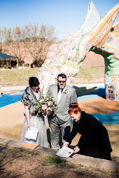 Nashville wedding officiant signing marriage license at Game of Thrones wedding under dragon arbor with bride wearing a silver dress and grey fur wrap and groom in a grey suit