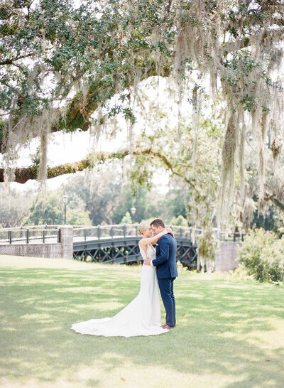 bride and groom standing under oak with Spanish moss while they embrace