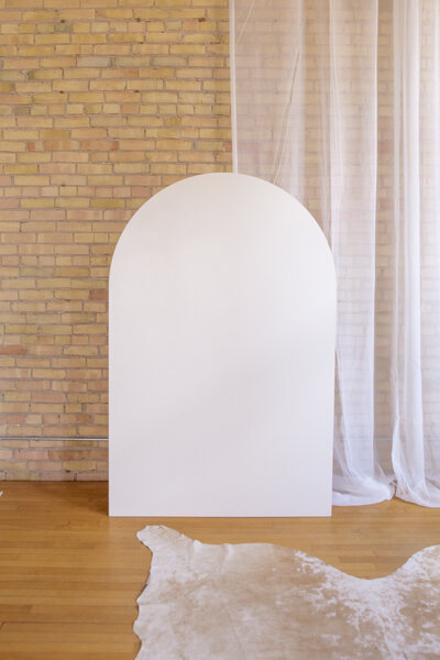 Six foot white wooden arch backdrop against a brick wall.