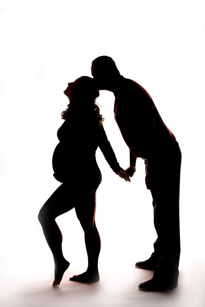 Dramatic silhouette maternity portrait featuring an expectant couple holding hands, captured in Overland Park, Kansas. A creative and intimate example of maternity photography for families in the Kansas City metro area.