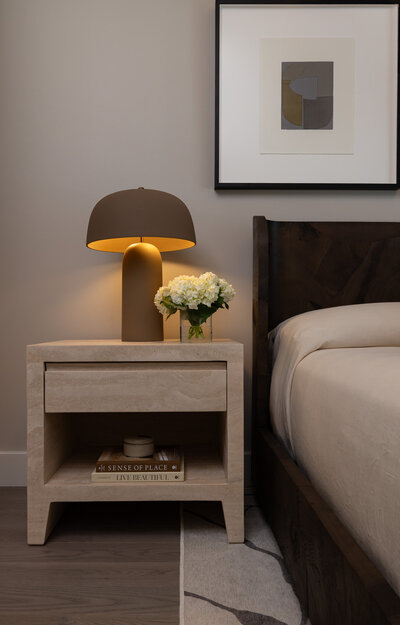 Close-up of a burlwood bed and travertine nightstand with a sculptural lamp and styled decor in the primary bedroom, designed by Sister Studio.
