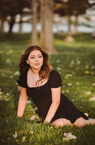 senior high school student sitting in grass with black dress posing for photo