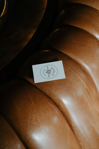 Logo design for a wedding industry professional on a white business card on top of a brown tufted leather couch