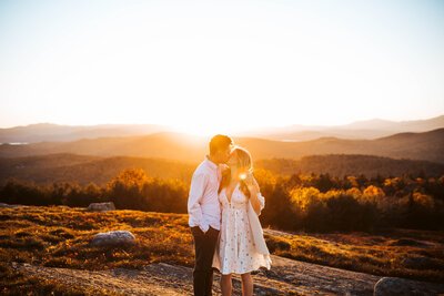 A couple kissing during golden hour on top of a mountain. 