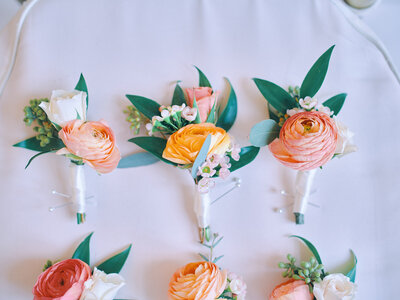 Coral flowers and greenery boutonnieres on a white background