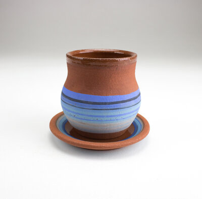 A red clay cup and matching plate decorated like a blue zarape style mexican blanket