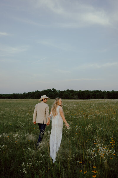 bride and groom walking through a wildflower field at their wedding venue near okc
