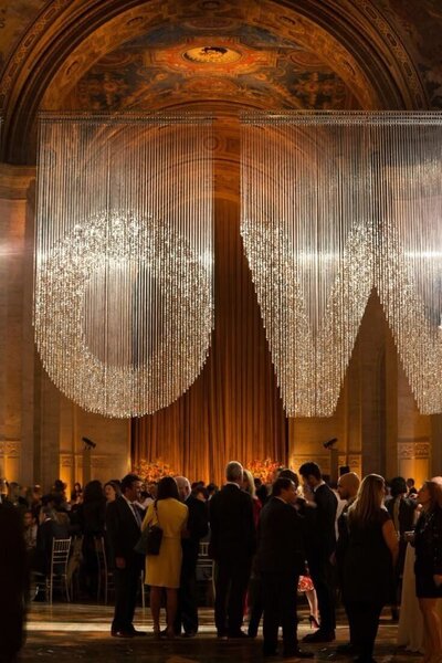 People socializing under a crystalline "NOW" display in a grand, ornate hall.