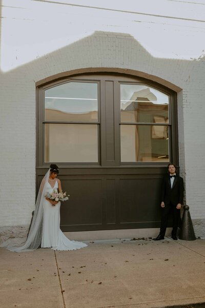 Couple in wedding attire standing against a white brick wall in downtown Portland, OR 