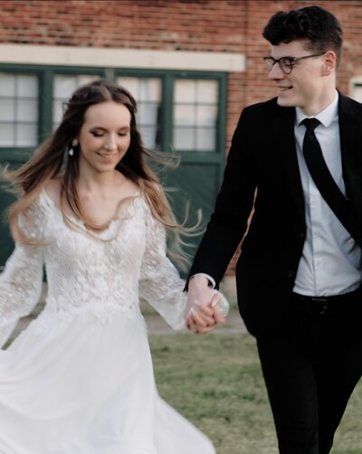 Couple runs through field in wedding outfits