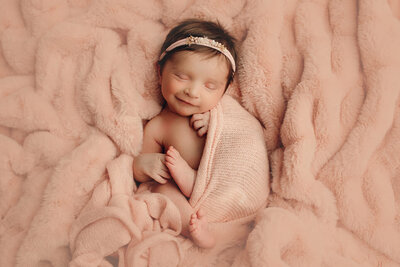 Girl sleeping on pink blanket wrapped up and smiling