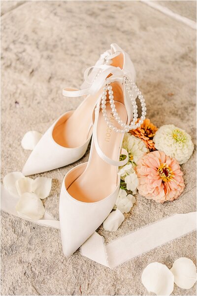 white bridal shoes surrounded with cream ribbon and  flowers