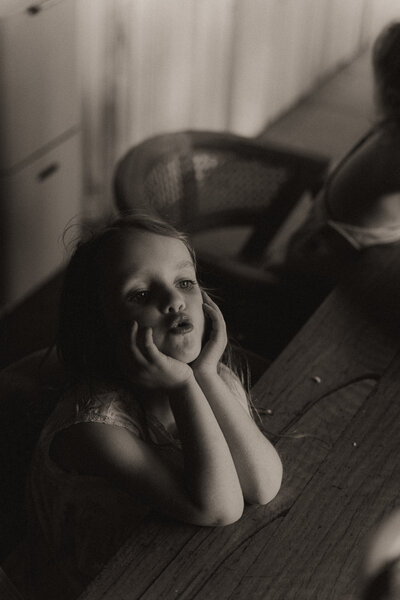 A film-like black and white photo of a little girl leaning on a table in her family photography session with Coffs Harbour photographer Fire & Fly