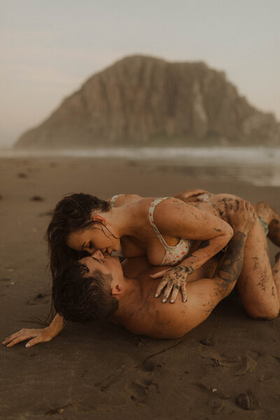 couple laying down in the sand kissing