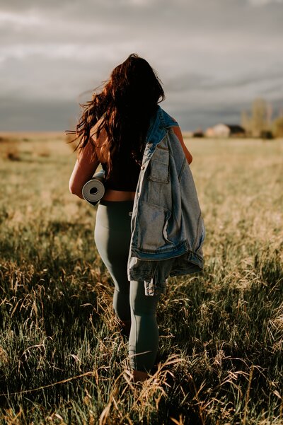woman walking through a saskatchewan field with yoga mat 