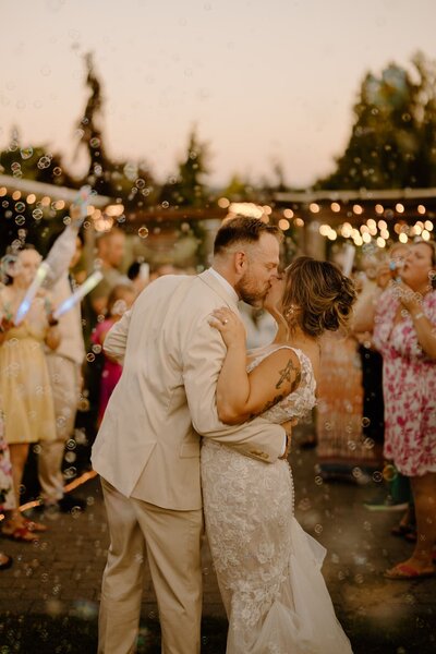Bride and groom kissing in a busy wedding setting surrounded by bubbles