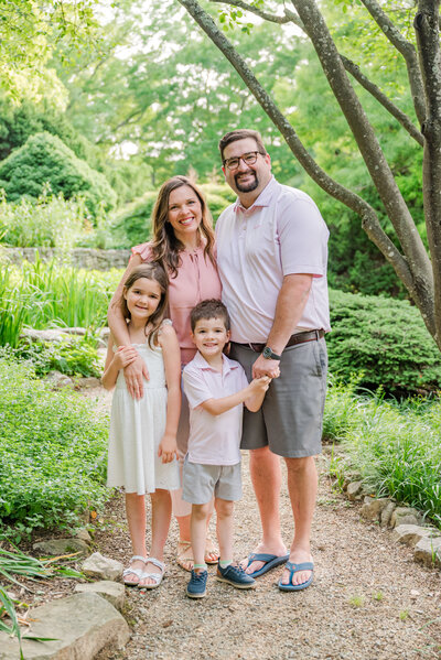 Family with 2 adults and 2 kids standing together in a botanical garden smiling