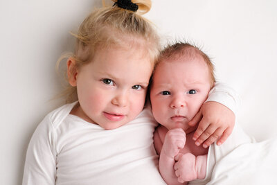 Intieme foto van een trotse grote zus die haar pasgeboren broertje vasthoudt. Een waardevolle herinnering uit een newborn shoot aan huis.