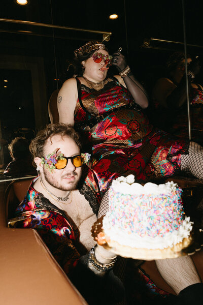 An queer wedding couple holding some cake dressed to match