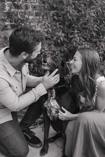man and woman kneeling down next to their dog while they both smile