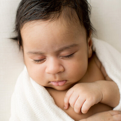 Sleeping baby with squishy cheeks is wrapped in a white blanket at Julie Brock Photography studio in Louisville KY