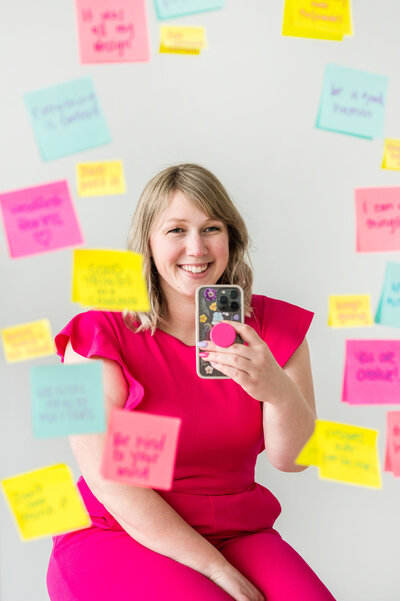 Kat Murphy taking a mirror selfie in front of a mirror covered in colorful sticky notes