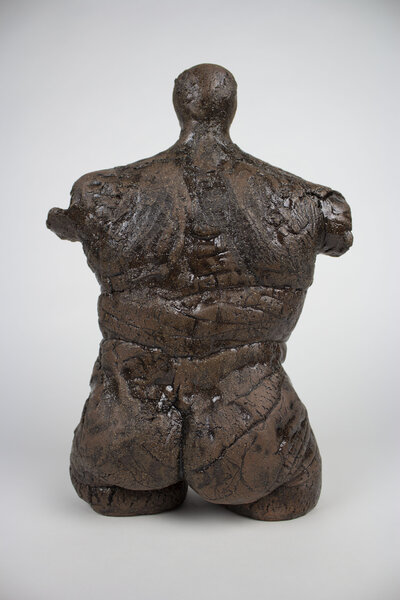 A ceramic bust of a feminine body with various cracks and brick textures