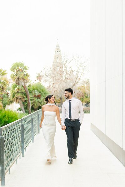 Engaged couple laughing and walking hand-in-hand next to Balboa Park's Timken Museum of Art.