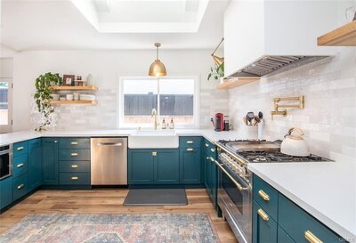 Spanish Revival-style kitchen with bold blue cabinets, gold hardware, gourmet appliances, white subway tile, and eclectic plant styling.