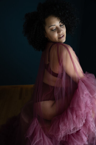 Elegant woman in a flowing purple tulle dress looking over her shoulder with a soft smile, against a dark backdrop