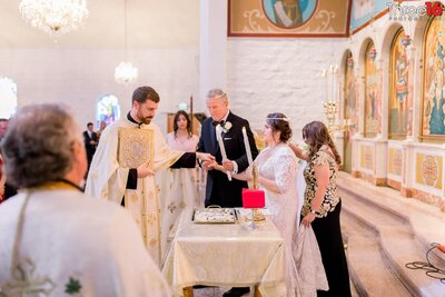 Officiant performs a Greek Orthodox wedding ceremony as the Bride and Groom stand in front of him
