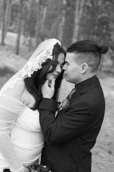 A bride and groom touch foreheads and close their eyes as he holds her chin with his hand.