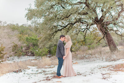 engaged to be married  couple posing forehead to forehead holding hands standing in the snow in the trees  with velvet dress by New Braunfels Photographer Firefly Photography