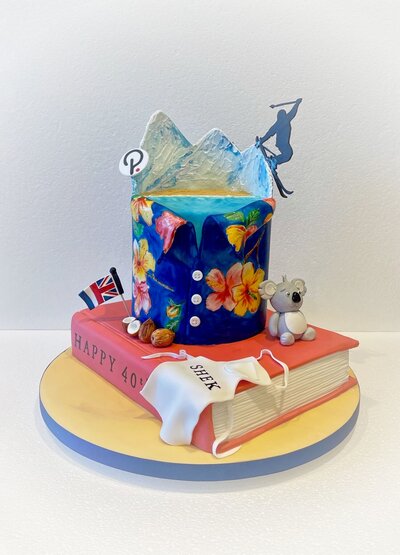 A custom birthday cake with a book, apron, koala, flag and floral shirt