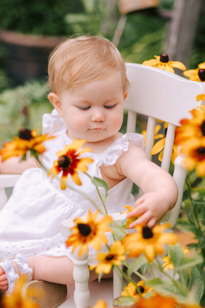 Little girl in a white dress looking at yellow flowers